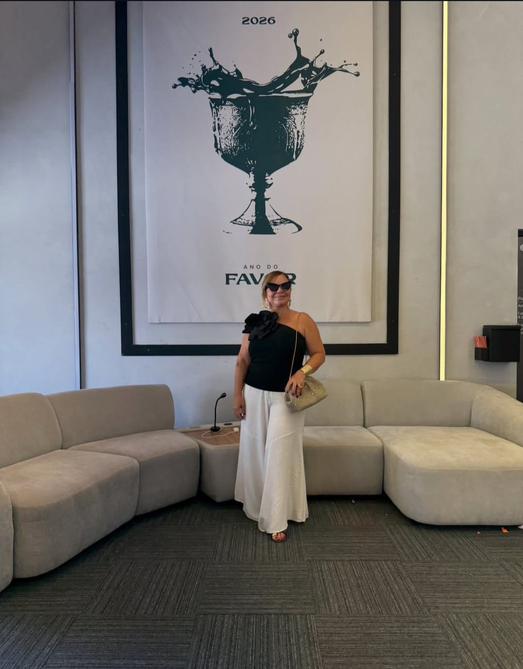 Sandra Martins em um salão moderno diante de um cartaz '2026 — Ano do Favor'